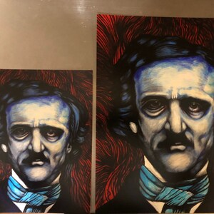 May include: Two framed prints of a portrait of Edgar Allan Poe. The portrait is a dark blue and white illustration of Poe with a dark blue background. The background of the larger print is a red and black abstract design. The background of the smaller print is a red and black abstract design.