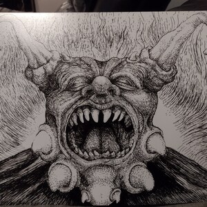 May include: A black and white pen and ink drawing of a grotesque, demonic creature with a large, open mouth and sharp teeth. The creature has horns and a large, bulbous nose.