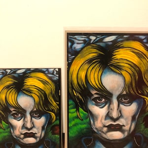 May include: A framed illustration of a woman with blonde hair. The woman is looking directly at the viewer with a serious expression. The background is a blue and green landscape.