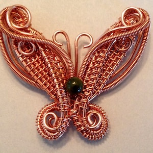 May include: A copper wire butterfly with a green stone in the centre. The butterfly's wings are made of intricate wirework.