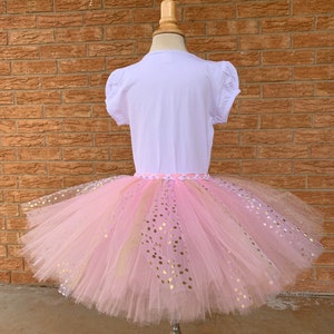 May include: A pink tulle tutu skirt with gold glitter polka dots. The skirt is on a white mannequin.