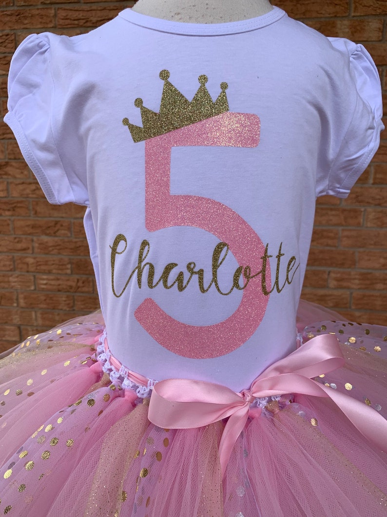 May include: A pink and gold tutu with gold polka dots and a pink satin bow. A white t-shirt with a pink number 5 and a gold crown, and the name Charlotte in gold glitter.
