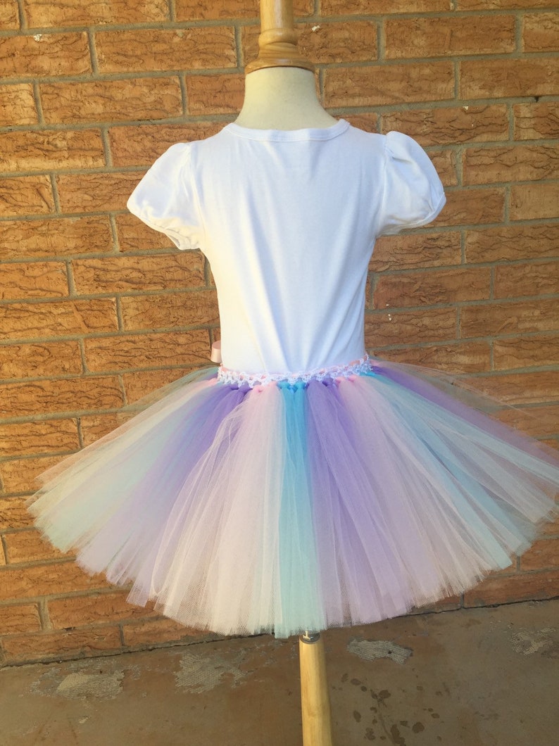 Peut inclure: Un t-shirt blanc avec une jupe tutu en tulle multicolore. La jupe est compos&eacute;e de plusieurs couches de tulle rose, bleu et violet.