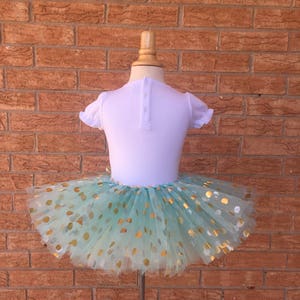 May include: A mint green tulle tutu skirt with gold polka dots. The skirt is on a white mannequin.