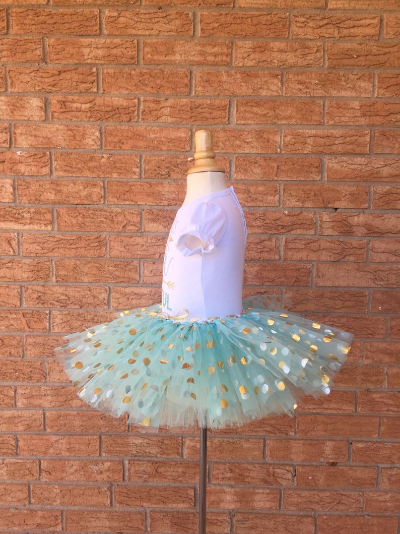 May include: A light blue tulle tutu with gold polka dots. The tutu is on a white dress form.