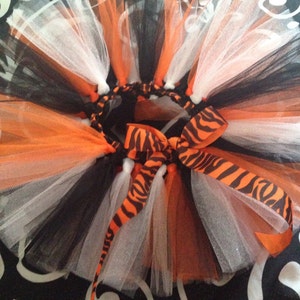 May include: A black, white, and orange tulle tutu with a zebra print ribbon. The tutu is layered and has a fluffy, full look.