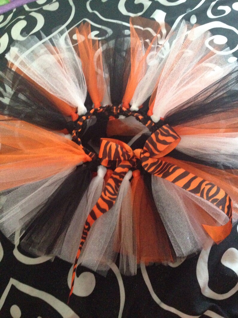 May include: A black, white, and orange tulle tutu with a zebra print ribbon. The tutu is layered and has a fluffy, full look.