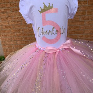 May include: A pink tulle tutu skirt with gold glitter polka dots. A white t-shirt with a pink number 5 and a gold glitter crown on top of the number. The name Charlotte is written in cursive below the number.