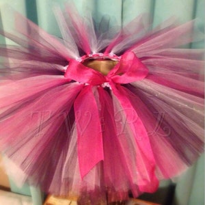 May include: A pink, white, and black tulle tutu with a pink satin ribbon tied around the waist.