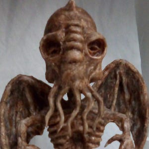 May include: A brown, detailed sculpture of a creature with a humanoid head, large eyes, and tentacles. The sculpture has large, leathery wings and a skeletal torso. The overall design suggests a mythical or fantasy theme.