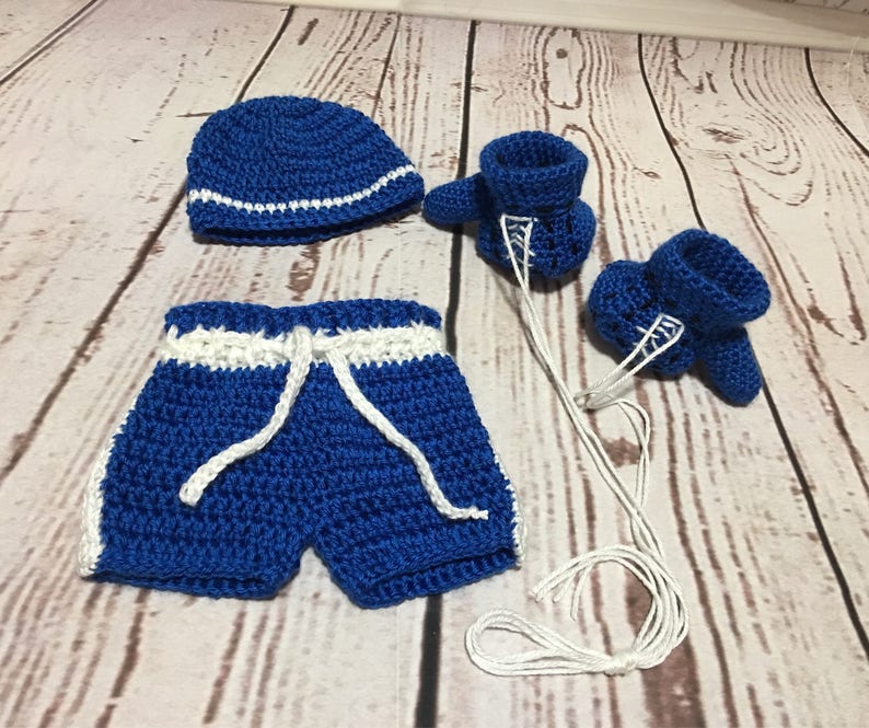 Puede incluir: Un conjunto de boxeo para beb&eacute; tejido a crochet en azul real con detalles blancos. El conjunto incluye un gorro, pantalones cortos con cord&oacute;n y guantes de boxeo. El gorro tiene una raya blanca. Los pantalones cortos tienen ribetes blancos. Los guantes tienen cordones blancos.