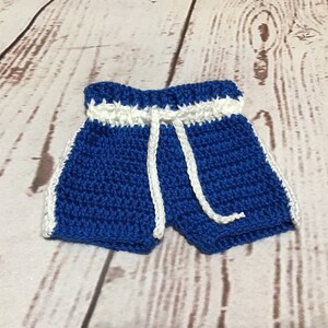 Puede incluir: Pantalones cortos de ganchillo azules hechos a mano con ribete blanco y un cord&oacute;n blanco. Los pantalones cortos est&aacute;n hechos con una puntada apretada y tienen un aspecto deportivo. Los pantalones cortos son probablemente para un beb&eacute; o un ni&ntilde;o peque&ntilde;o.
