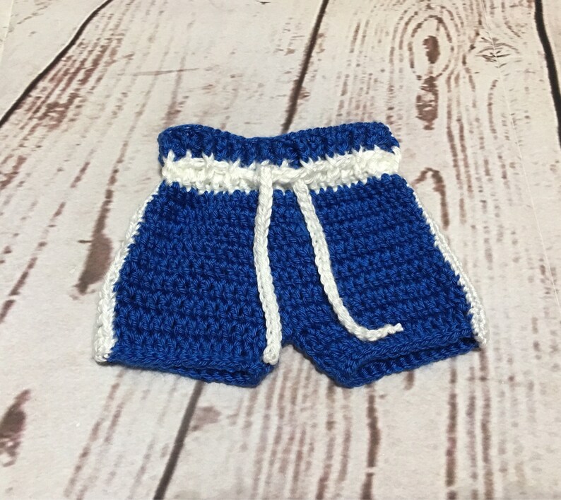 Puede incluir: Pantalones cortos de ganchillo azules hechos a mano con ribete blanco y un cord&oacute;n blanco. Los pantalones cortos est&aacute;n hechos con una puntada apretada y tienen un aspecto deportivo. Los pantalones cortos son probablemente para un beb&eacute; o un ni&ntilde;o peque&ntilde;o.