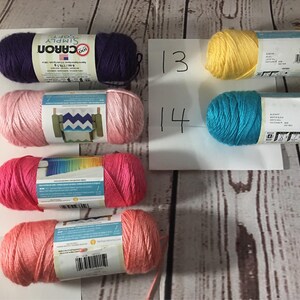 Puede incluir: Surtido de ovillos de hilo Caron Simply Soft en varios colores, incluyendo morado, rosa, coral, amarillo y turquesa. El hilo est&aacute; dispuesto sobre una superficie clara con vetas de madera, con etiquetas de papel blanco numeradas.