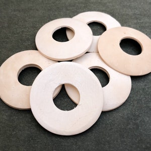 May include: Six off-white round ceramic or porcelain bottle stoppers with a hole in the center. The stoppers are stacked on top of each other.