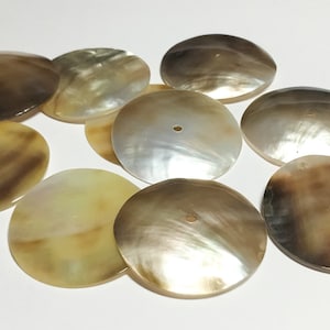 May include: A collection of eight round, iridescent, mother-of-pearl shell buttons with a hole in the center. The buttons are various shades of brown and beige.