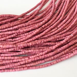 May include: A strand of pink, round, and slightly flat beads. The beads are made of natural materials and have a rustic, organic look.