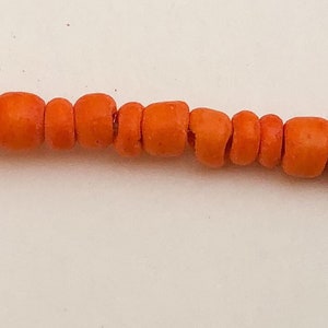 May include: A strand of orange coral beads. The beads are round and smooth, and they are strung together on a clear thread.