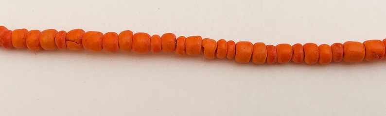 May include: A strand of orange coral beads. The beads are round and smooth, and they are strung together on a clear thread.