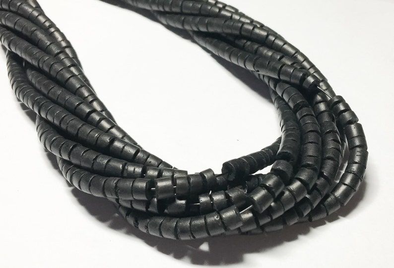May include: A strand of black, round, and slightly coiled beads. The beads are made of a natural material and have a matte finish.