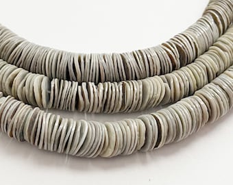 Op de afbeelding: Drie strengen grijze, platte, schijfvormige kralen. De kralen hebben een natuurlijk, organisch uiterlijk met variaties in kleur en textuur. De kralen zijn aan elkaar geregen, waardoor een ketting of armband ontstaat.