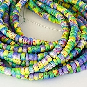 May include: A close-up of a multi-colored string of beads. The beads are small and round, and they are made of a white material with a speckled finish. The beads are in shades of green, blue, yellow, and purple.