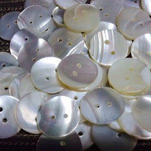 May include: A collection of white mother of pearl buttons with two holes each. The buttons are round and have a smooth, shiny finish.