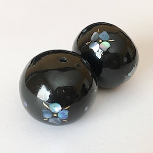以下が含まれることがあります： 花柄の黒い丸いビーズが2つ。花は虹色の素材でできており、青と白の色をしています。