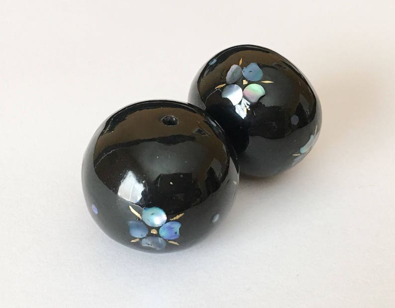以下が含まれることがあります： 花柄の黒い丸いビーズが2つ。花は虹色の素材でできており、青と白の色をしています。