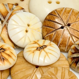 May include: A collection of various wooden buttons in shades of cream and brown. The buttons feature carved designs, including radial patterns and leaf-like textures. Some buttons have two or four holes for sewing.