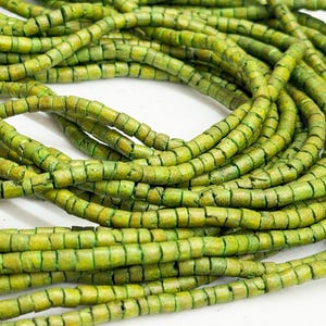 May include: Close-up of a pile of green beads. The beads are cylindrical with a segmented appearance, and they have a slightly weathered, textured look. The color is a mix of light and dark greens.