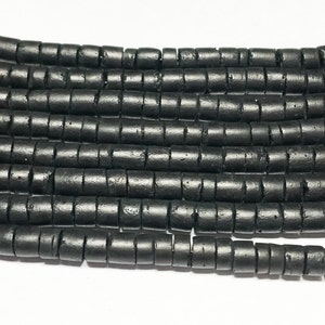 May include: Black wooden beads, each bead is a cylinder with a grooved texture. The beads are arranged in rows, creating a visual pattern.