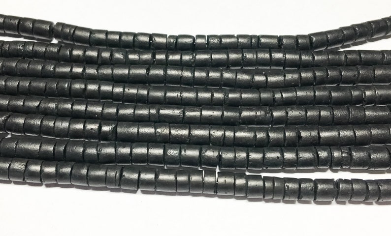 May include: Black wooden beads, each bead is a cylinder with a grooved texture. The beads are arranged in rows, creating a visual pattern.