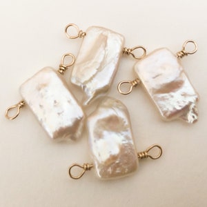 May include: Five white baroque pearl charms with gold-toned jump rings. The pearls are irregular in shape and have a slightly iridescent sheen.