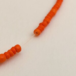 May include: Close-up of a string of orange beads strung on a clear thread. The beads are round and have a smooth, polished finish.