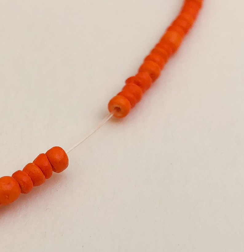 May include: Close-up of a string of orange beads strung on a clear thread. The beads are round and have a smooth, polished finish.