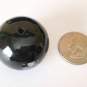 以下が含まれることがあります： 中央に小さな穴のある黒いセラミック球体。球体は光沢のある仕上げで、白と青の微妙なアクセントが施されています。