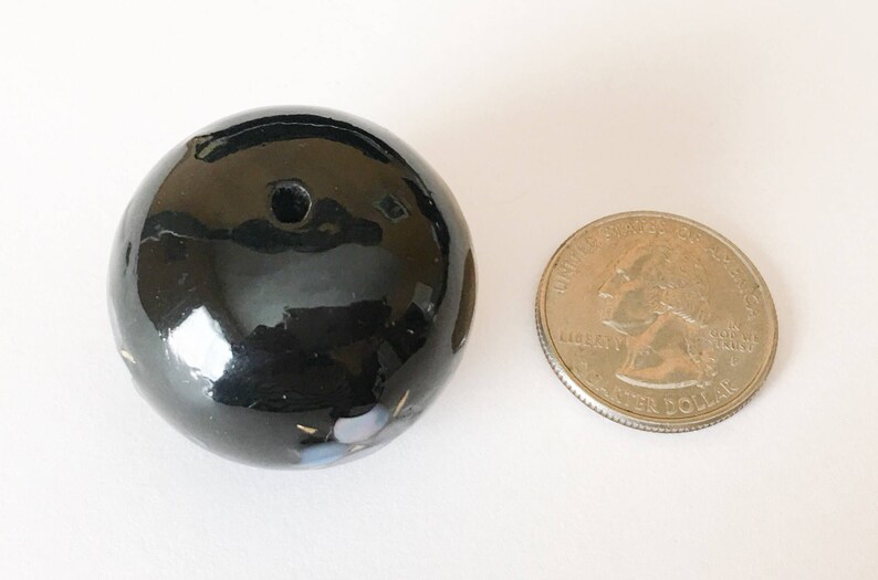 以下が含まれることがあります： 中央に小さな穴のある黒いセラミック球体。球体は光沢のある仕上げで、白と青の微妙なアクセントが施されています。