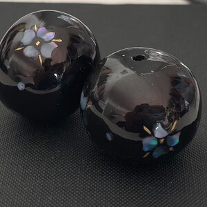 以下が含まれることがあります： 虹色の花柄が施された黒いセラミック製の球体2つ。球体は滑らかで光沢があります。