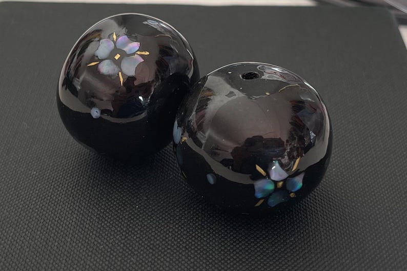 以下が含まれることがあります： 虹色の花柄が施された黒いセラミック製の球体2つ。球体は滑らかで光沢があります。