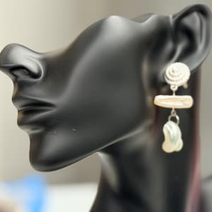 May include: A pair of earrings displayed on a black mannequin head. The earrings feature a silver spiral stud, a rectangular pearl, and a teardrop-shaped pearl pendant. The pearls have a creamy white color.