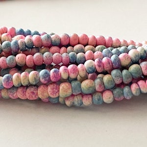 May include: A strand of small, round beads in shades of pink, blue, and white. The beads have a speckled, marbled appearance.