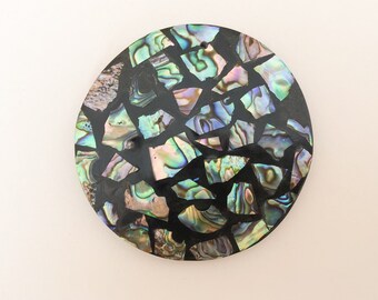 May include: A round, black, decorative coaster with a mosaic of iridescent green, blue, and purple abalone shell pieces.