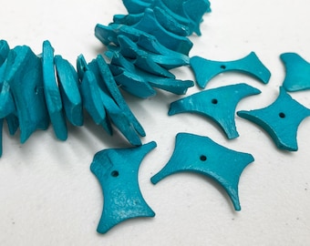 May include: Turquoise-colored wooden beads and decorative elements. The beads are irregularly shaped and strung together, while the other elements have a unique, geometric design with a hole in the center. The items are on a white surface.