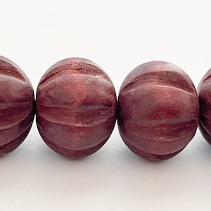 May include: A strand of dark red wooden beads with a carved, ribbed design. The beads are round and have a smooth, polished finish.