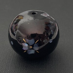 以下が含まれることがあります： 上部に小さな穴があり、青と金の虹色の花が装飾的にデザインされた黒いセラミック球体です。