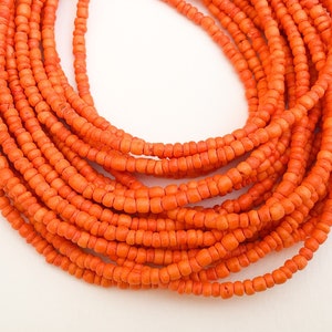 May include: A close-up of a long strand of orange beads. The beads are small and round, and they are strung together in a continuous line.