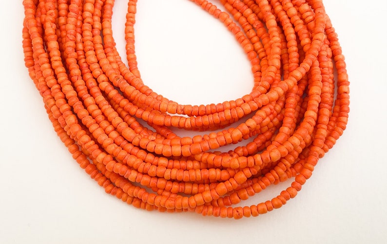 May include: A close-up of a long strand of orange beads. The beads are small and round, and they are strung together in a continuous line.