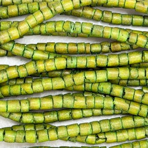 May include: Close-up of several strands of green and yellow wooden beads. The beads are cylindrical with a segmented design, creating a textured appearance. The beads are strung together, forming a necklace or bracelet.
