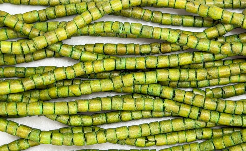 May include: Close-up of several strands of green and yellow wooden beads. The beads are cylindrical with a segmented design, creating a textured appearance. The beads are strung together, forming a necklace or bracelet.